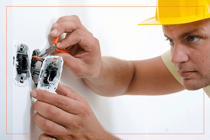 A person in yellow hard hat working on an electrical outlet.