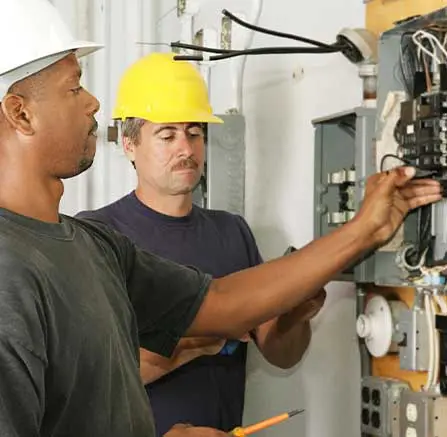 Two electricians working on electrical components indoors.